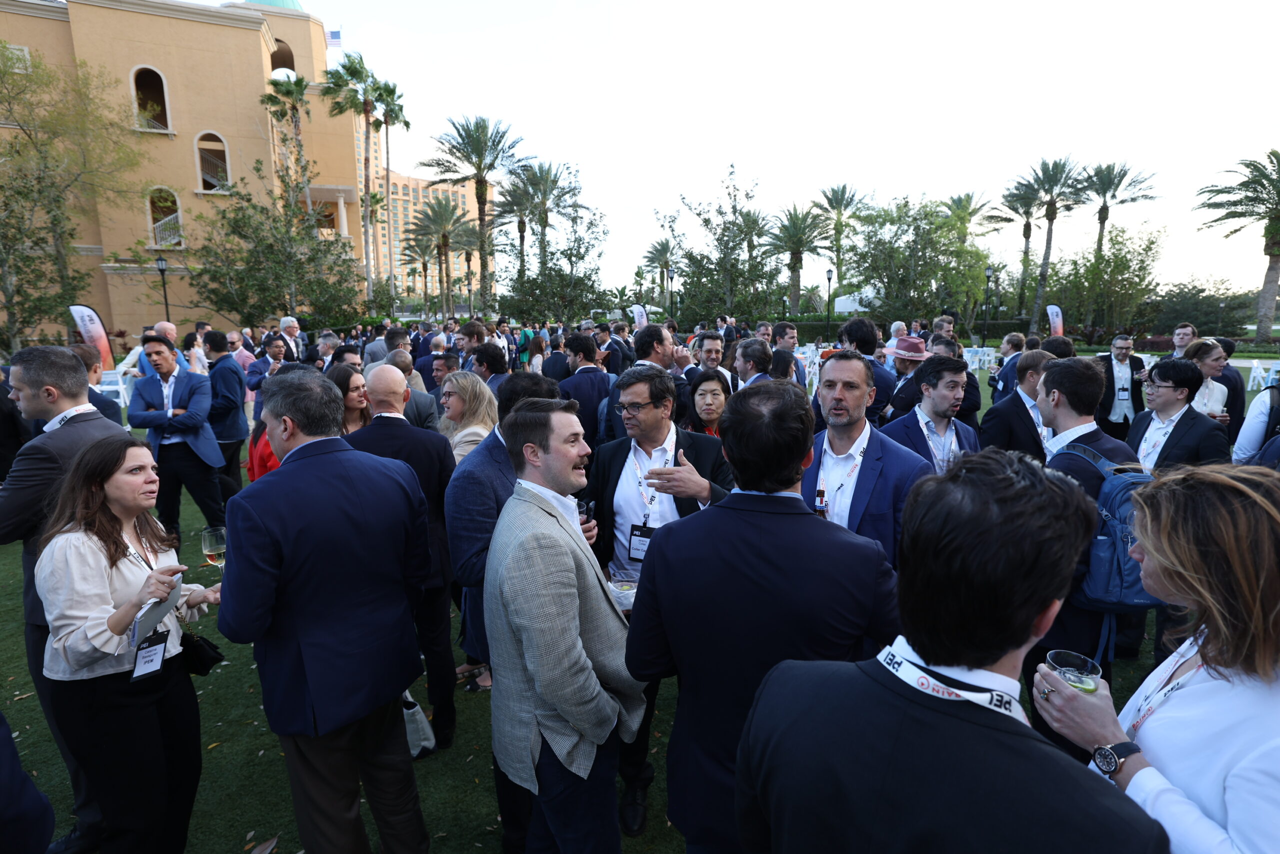 crowd of men and women mingling outdoors with palm trees